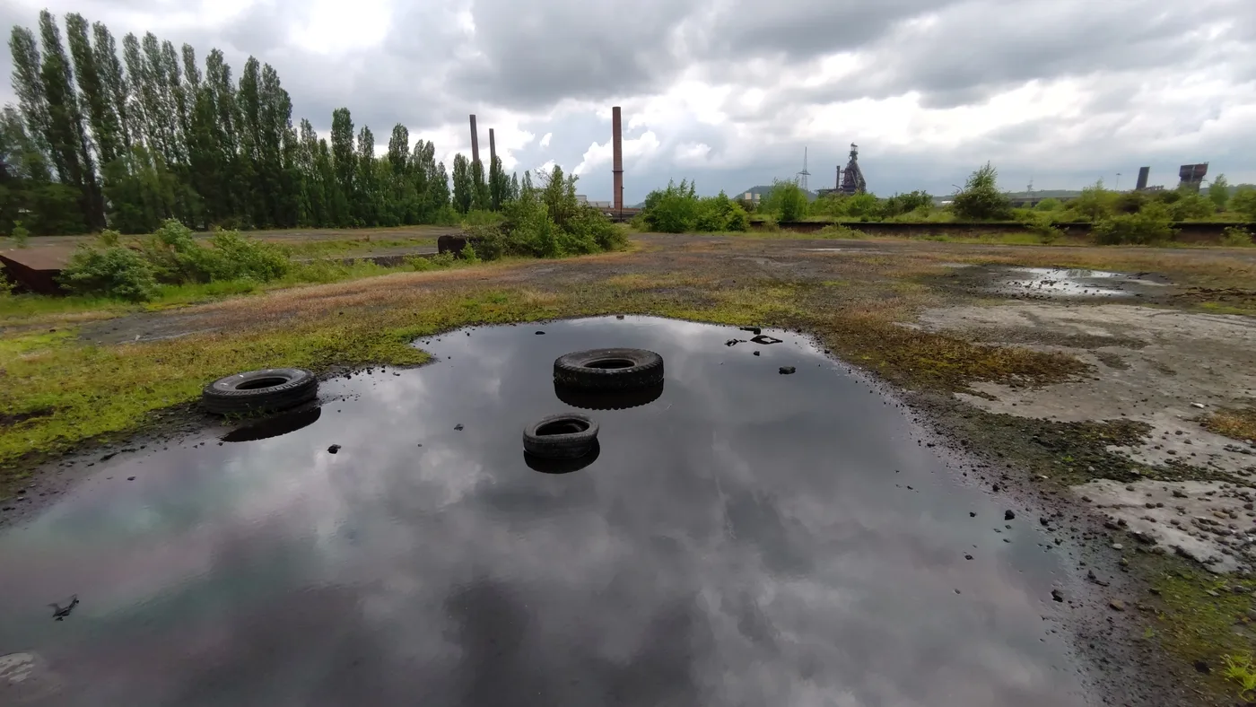 Post-industrial brownfield at the foot of the Charleroi slag heaps, with factory chimneys on the horizon