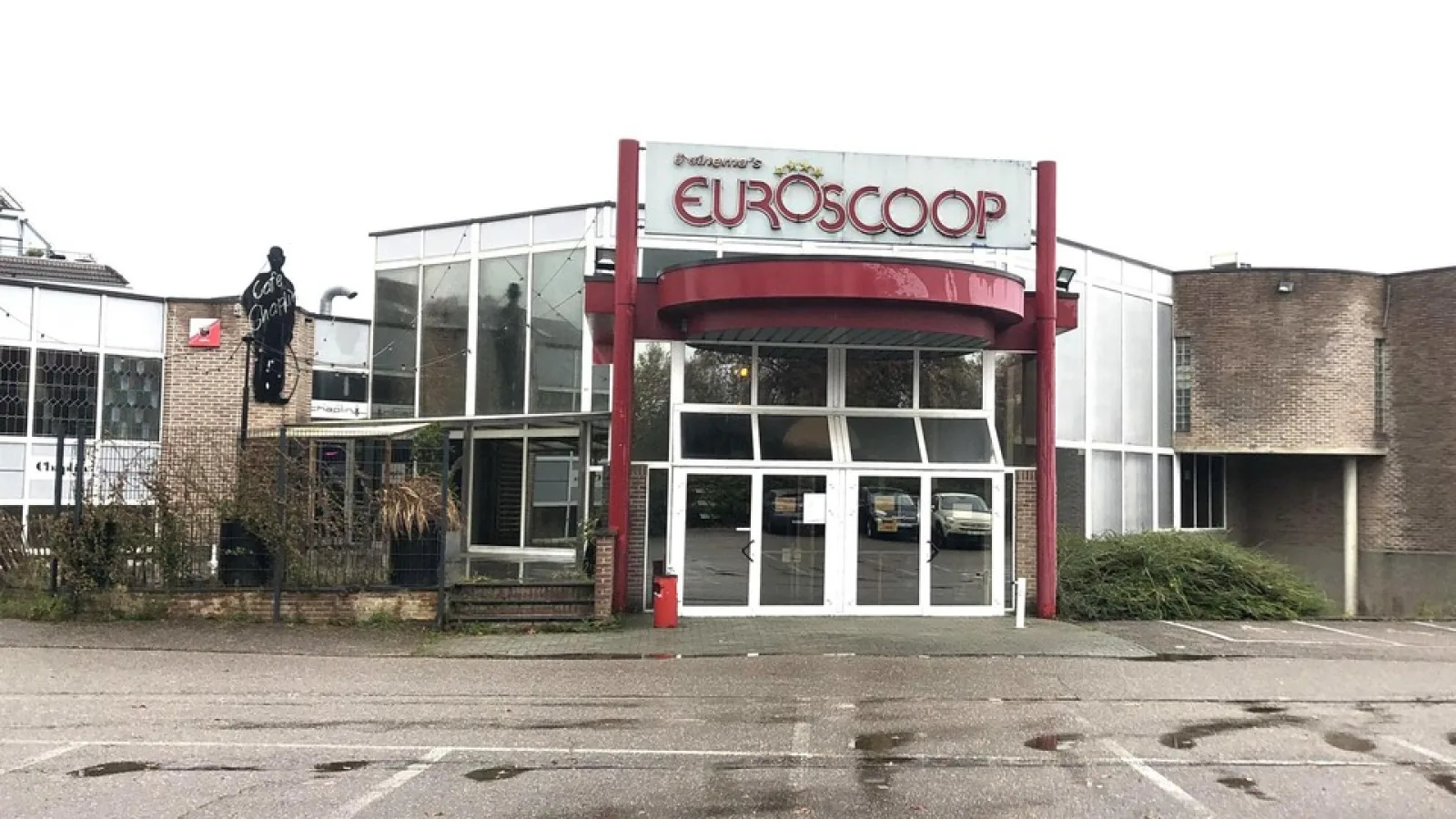 Abandoned entrance of the Euroscoop cinema complex in Lanaken, with the Euroscoop sign above the glass doors and an empty car park